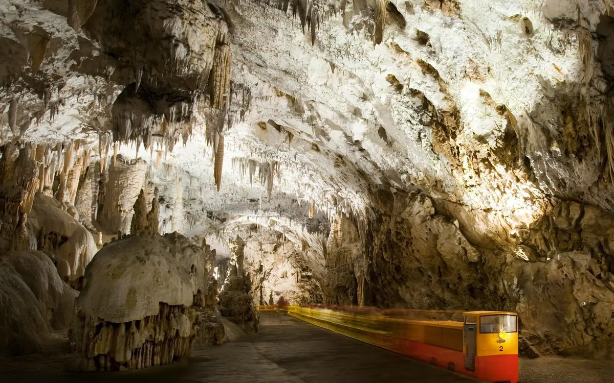 A railed walkway curving through a tall limestone chamber with warm lighting overhead