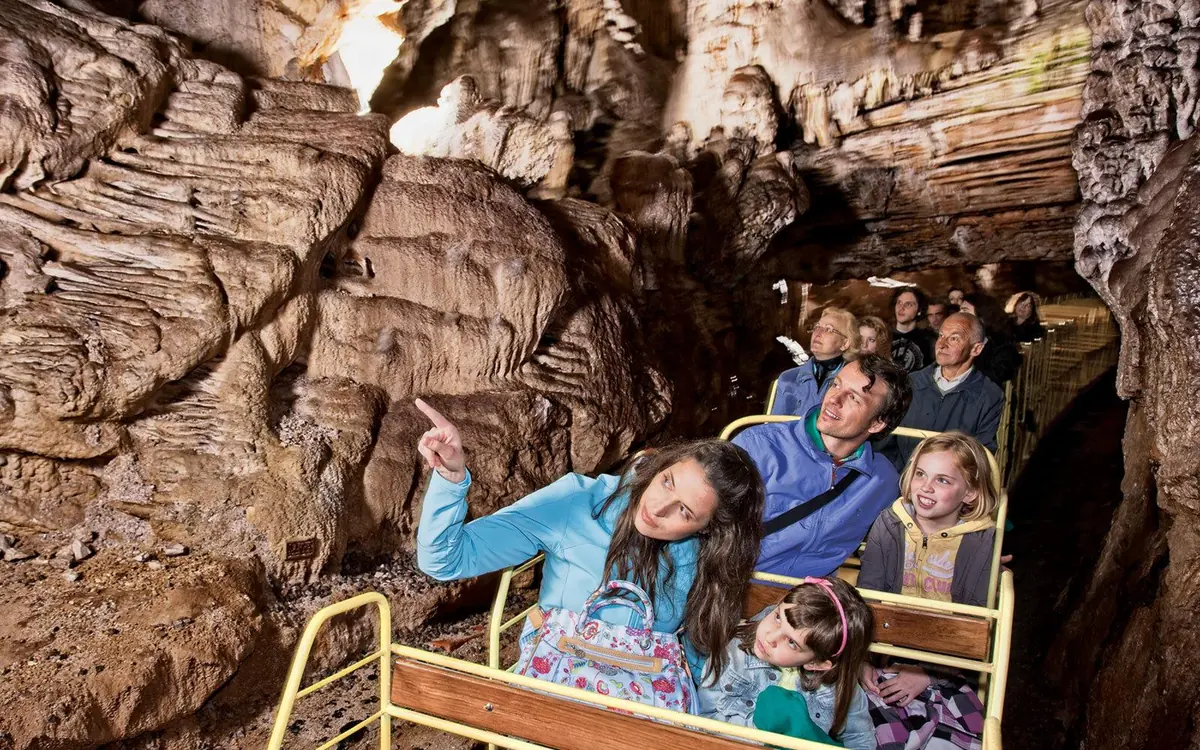 Children riding in an open carriage of the underground train inside Postojna Cave, one girl pointing up at the rock above them