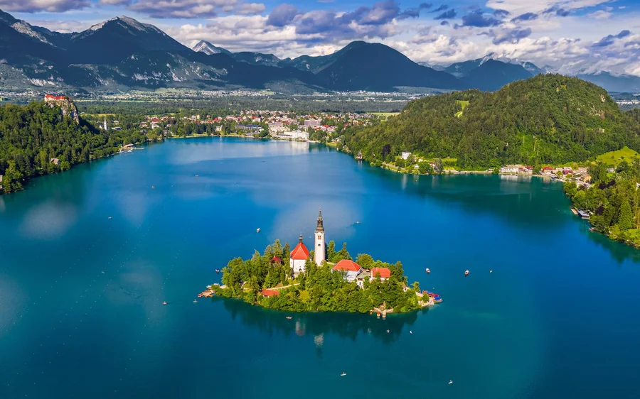 Lake Bled seen from a hillside, the island church on the water and green wooded slopes around it