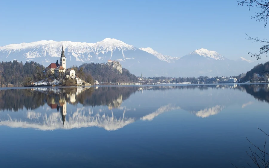 Lake Bled in winter, the island church mirrored in calm water below snow-covered mountains