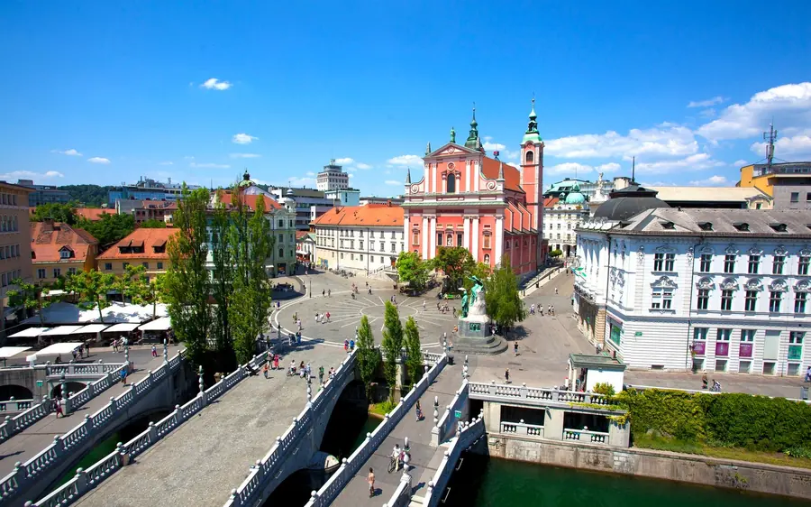 The riverside of Ljubljana with coaches parked along the embankment and the pink Franciscan church behind